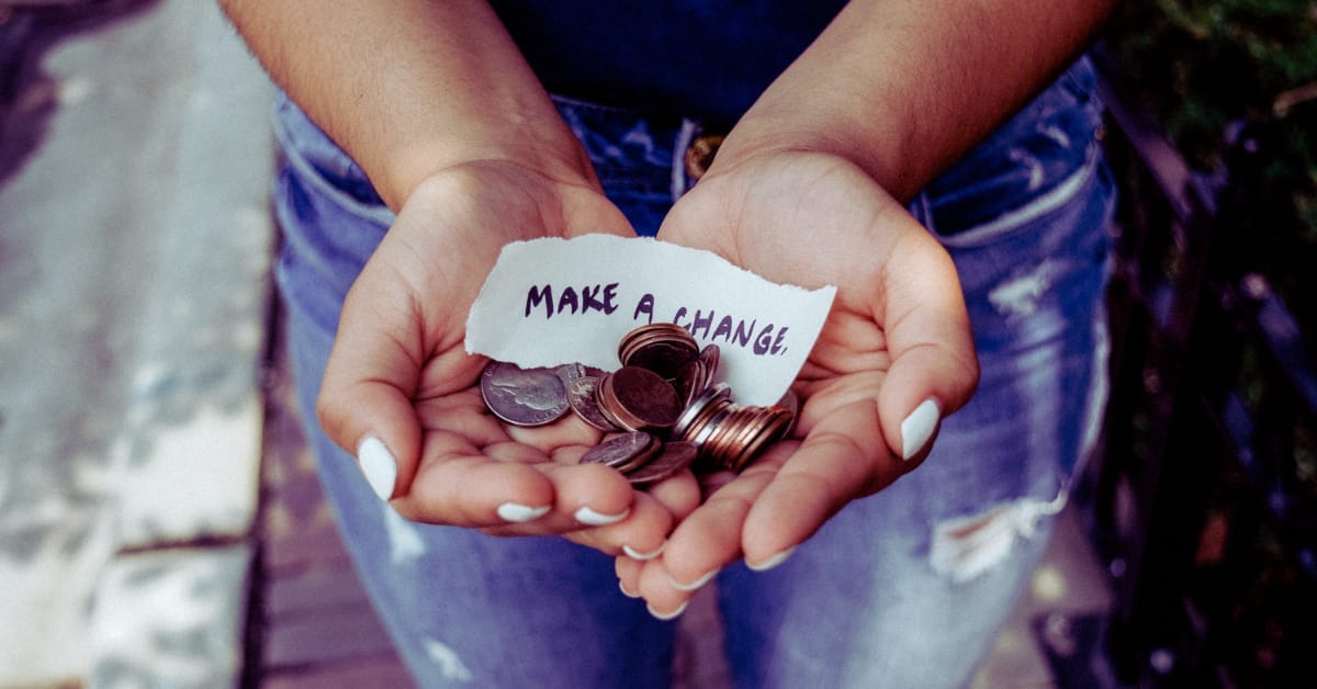 Person holding some coins with a handwritten paper "make a change"